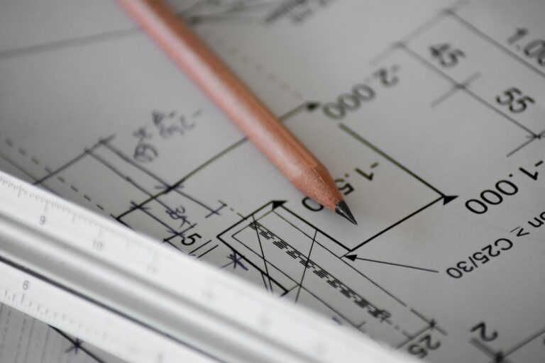 Ein brauner Bleistift liegt auf technischen Zeichnungen mit weissem Lineal im Vordergrund